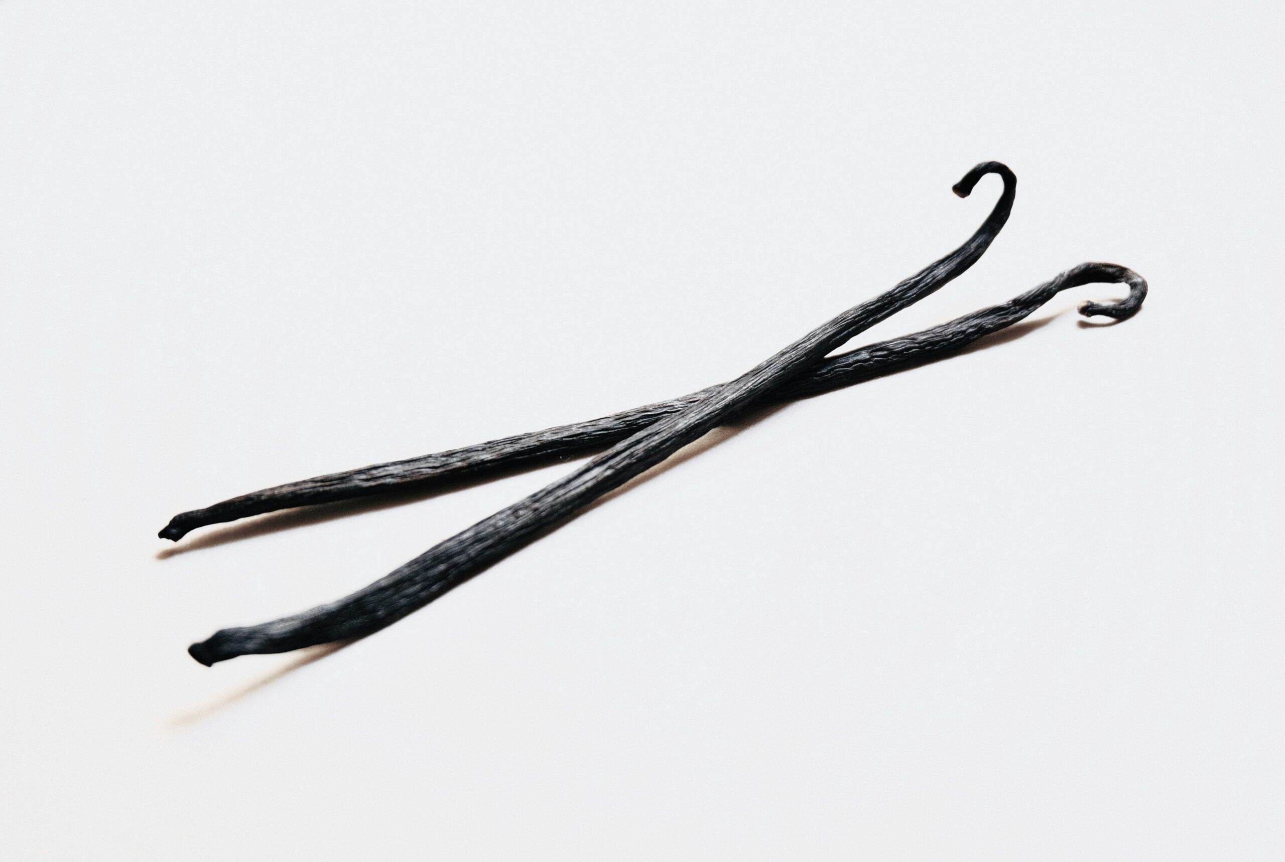 Two dark, dried vanilla beans arranged on a light background, showcasing their unique shape and texture, ideal for culinary uses and flavoring.